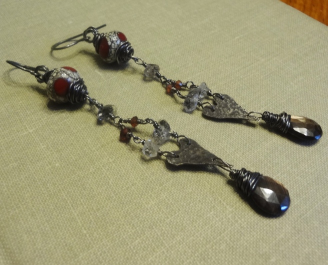 A pair of long earrings consisting of an ivory and red handmade bead, 3 clear herkimer diamonds, 2 red garnets, hand-cut sterling silver hearts, and black sapphire teardrops